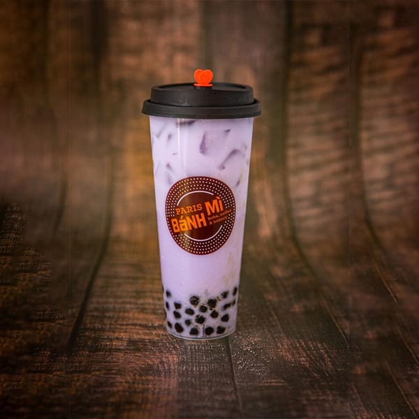 Taro boba tea with a Paris Bánh Mì logo and heart-shaped stopper on a wooden surface.