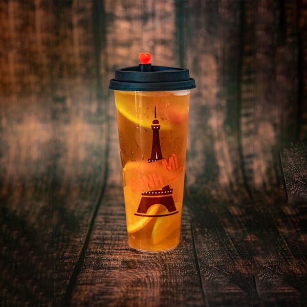 A clear plastic cup of iced tea with orange slices and a Paris Bánh Mì logo.