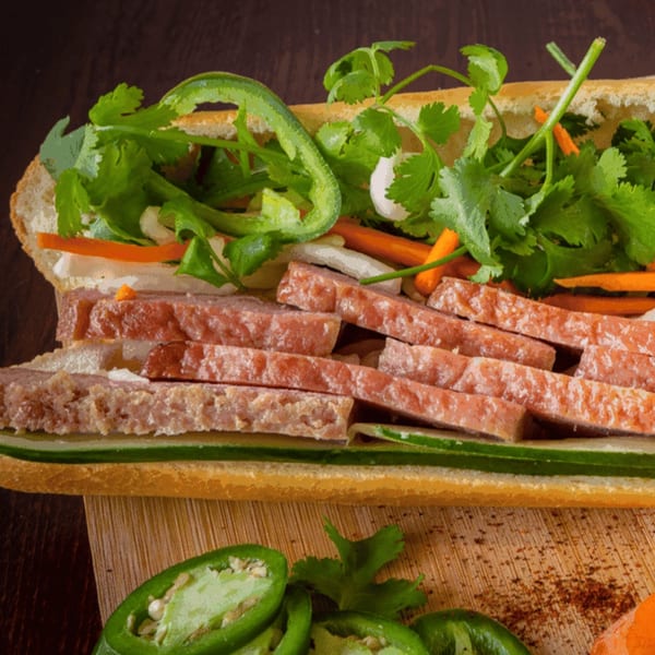 A Vietnamese bánh mì sandwich with sliced meat, cilantro, jalapeños, and pickled vegetables.