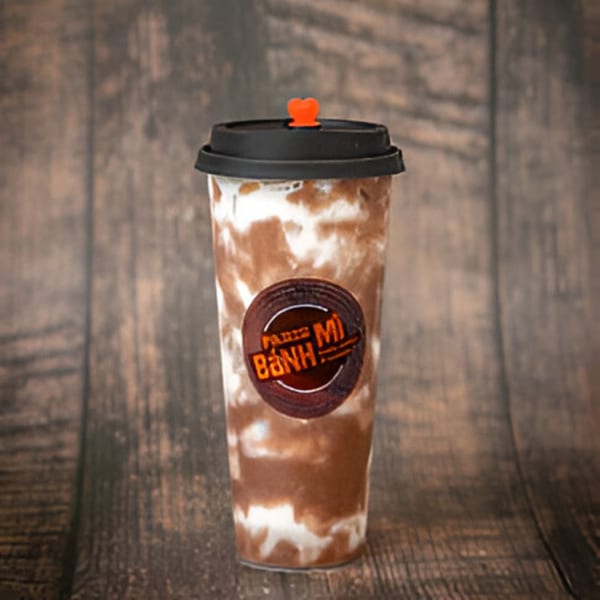 A Paris Bánh Mì iced coffee drink with a heart-shaped straw stopper on a wooden background.