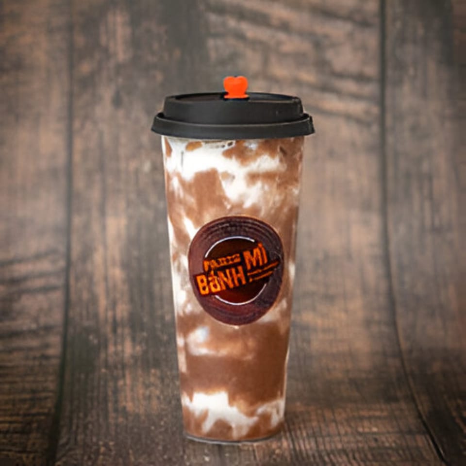 A Paris Bánh Mì iced coffee drink with a heart-shaped straw stopper on a wooden background.